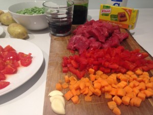 Ingredienti freschi e carne di manzo per spezzatino su un tagliere, inclusi pomodori, carote, aglio e vino rosso.