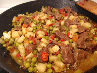 Un piatto di spezzatino di carne di manzo con patate, piselli e peperoni in un tegame.