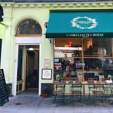 Facciata di Camellia's Tea House a Londra, con insegna verde e tavolini all'esterno.