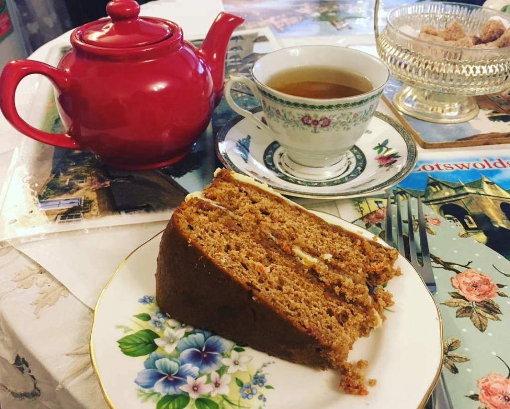 Una teiera rossa e una tazza di tè su un piatto decorato, accompagnate da una fetta di torta su un tavolo decorato con una tovaglia elegante.