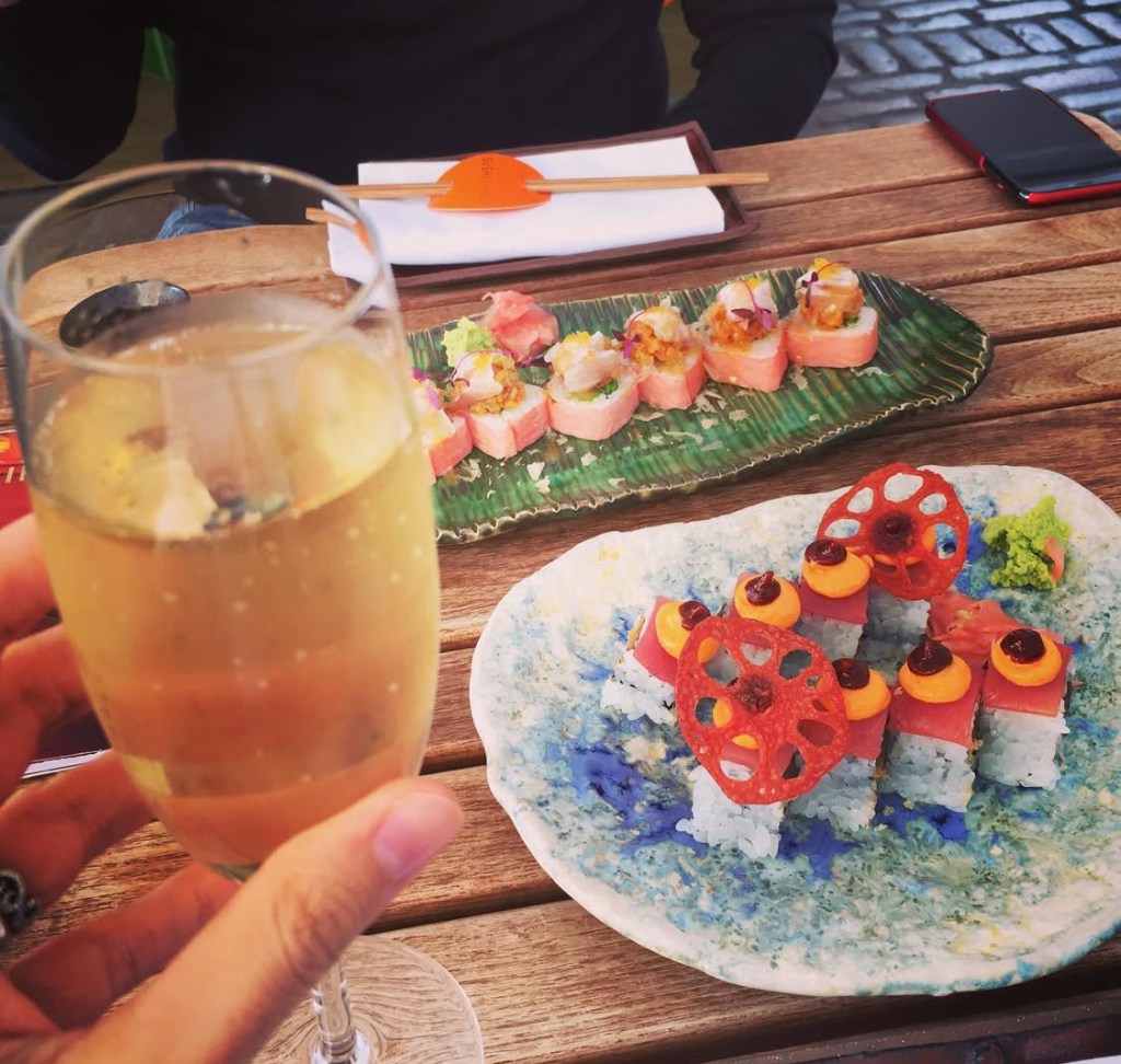Un bicchiere di champagne con dei piatti di sushi colorati disposti su un tavolo di legno al Sushi Samba di Londra.