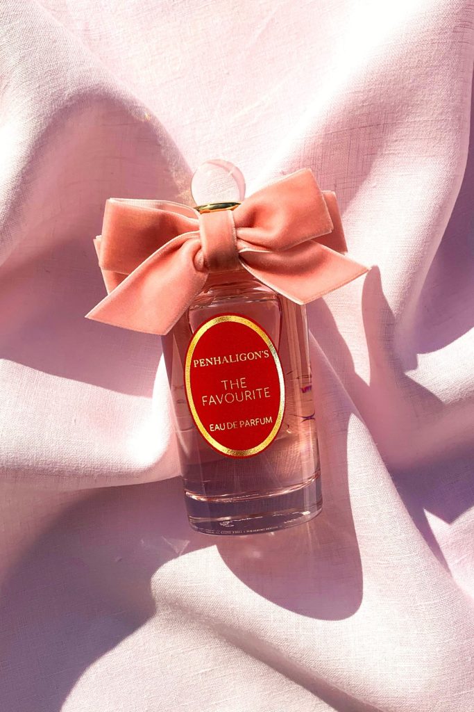 Flacone di profumo Penhaligon's 'The Favourite' con fiocco rosa su un fondo di tessuto chiaro.