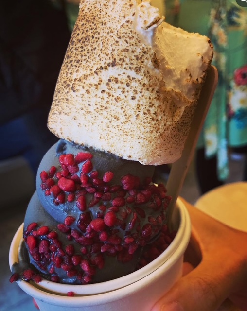 Un cono di gelato artigianale con uno strato di meringa croccante, decorato con piccoli pezzi di frutta rossa su una base di gelato scuro.