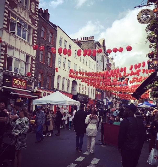 Una vivace strada di Londra decorata con lanterne rosse, affollata di persone e bancarelle che offrono cibo e prodotti locali.