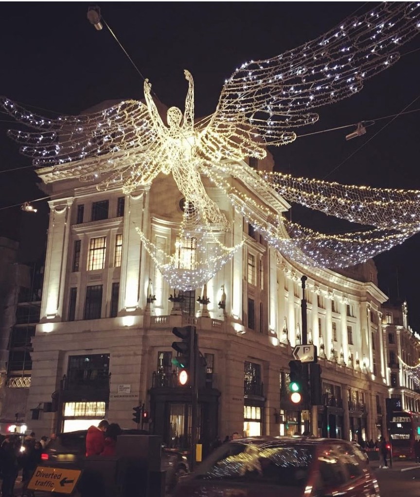 Decorazioni natalizie a Londra con un angelo illuminato sopra un edificio, mentre la città scintilla di luci festive.