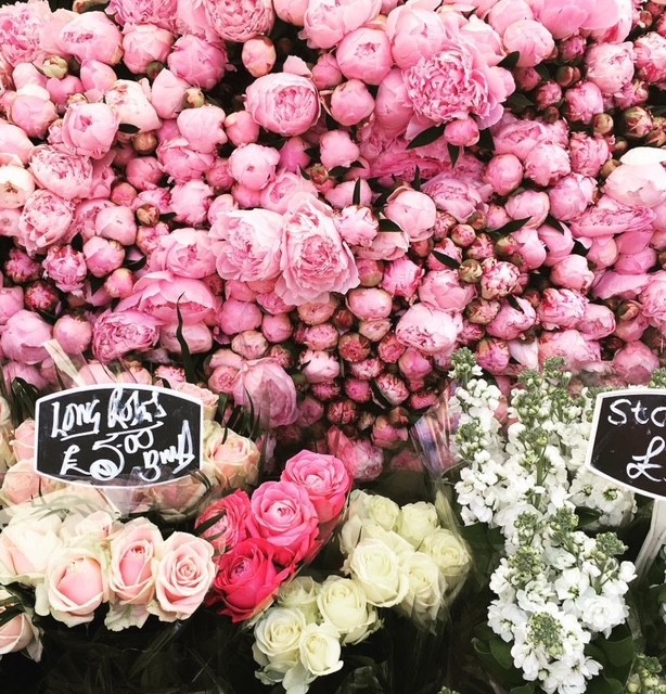 Un'esplosione di fiori freschi, con peonie rosa e rose bianche e colorate esposte in un mercato fiorito.