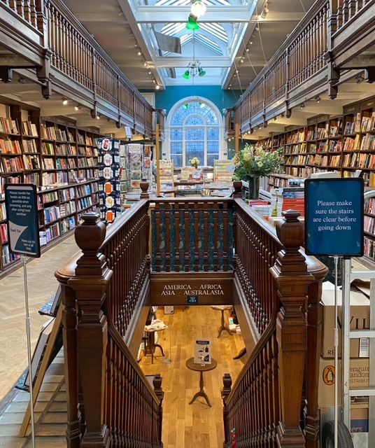 Interno della libreria Daunt molto elegante che sta a Londra, con scaffali di libri su entrambi i lati e un corridoio centrale con scale in legno e una grande finestra.
