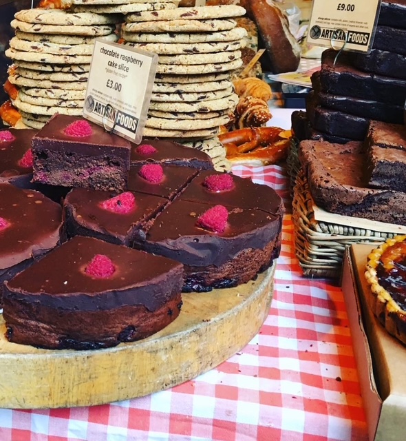 Fette di torta al cioccolato e lampone su un tavolo con biscotti, brownie e dolci in un mercato di street food.