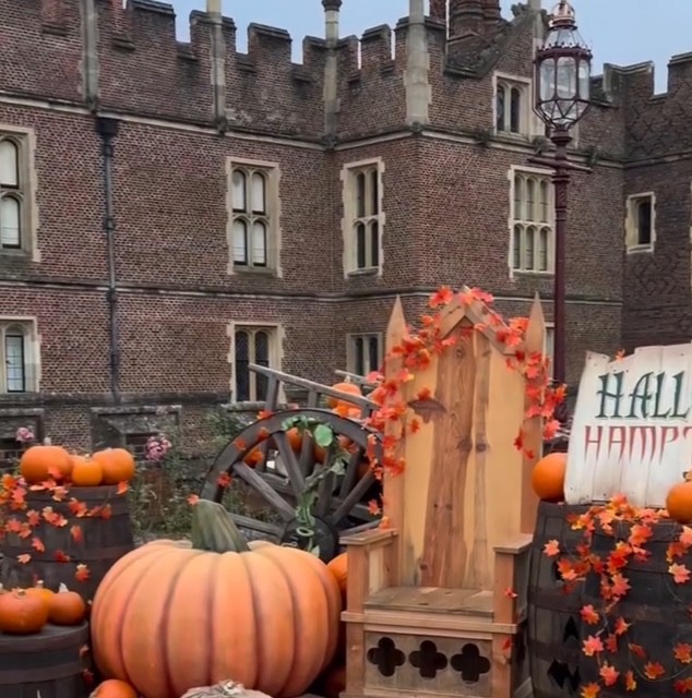 Decorazione autunnale di Halloween presso Hampton Court Palace, con una grande zucca, carrelli e ornamenti arancioni e rossi davanti a un edificio storico.