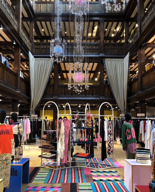 Interno di Liberty, un negozio di moda a Londra, con scaffali di abbigliamento e decorazioni eleganti, inclusi lampadari e tappeti colorati.