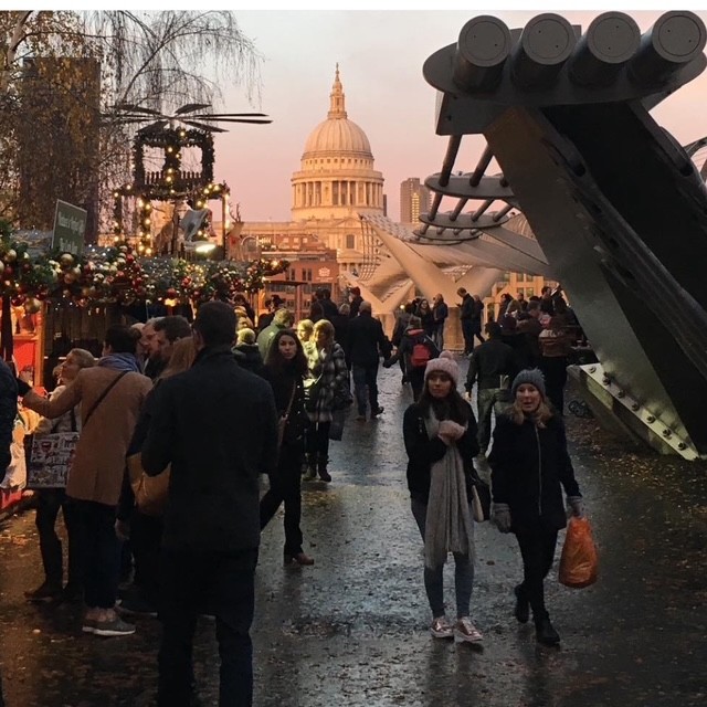 Una scena di un mercato all'aperto a Londra durante la sera, con persone che passeggiano, bancarelle decorate e la cattedrale di St. Paul sullo sfondo.