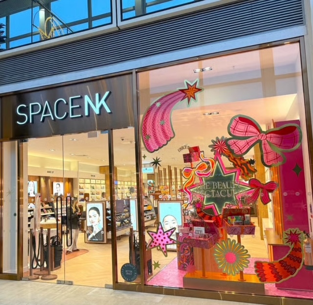Insegna e vetrina del negozio Space NK, elegante e colorata, con decorazioni artistiche e prodotti di bellezza visibili all'interno.