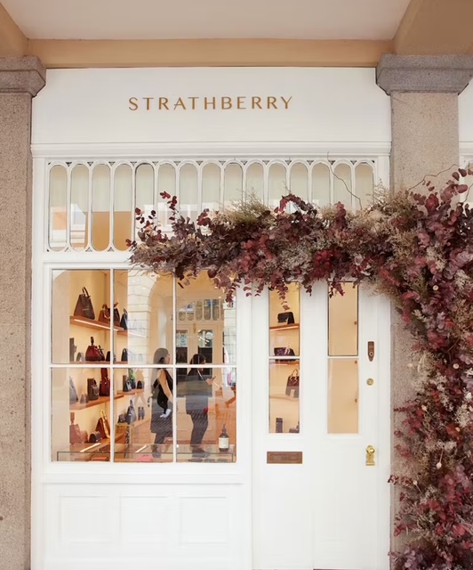 Insegna del negozio Strathberry con vetrina decorata e borse in esposizione.