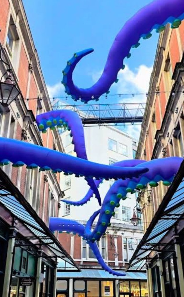 Un'installazione artistica di tentacoli viola appesi sopra una strada del centro di Londra, creando un'atmosfera suggestiva per Halloween.