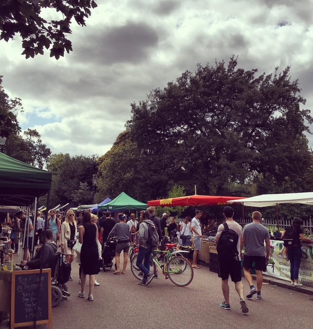 Mercato all'aperto affollato con banchi colorati e visitatori che passeggiano, sotto un cielo nuvoloso.