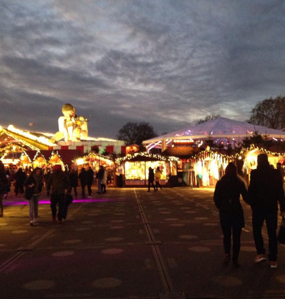 Un mercatino di Natale a Londra, con alberi decorati e luci, sotto un cielo nuvoloso al tramonto.
