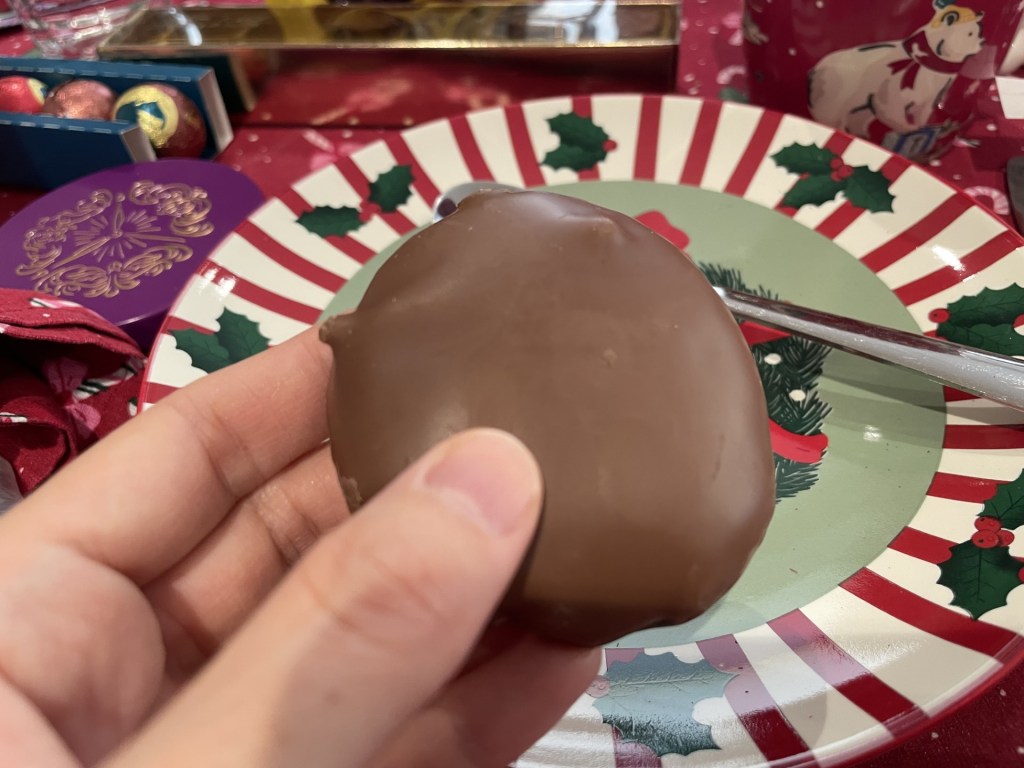 Un biscotto ricoperto di cioccolato tenuto in mano su un piatto decorato per il Natale.