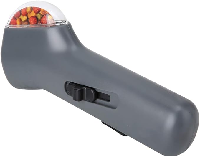 Un dispositivo manuale per dosare snack o cibo, con un'impugnatura grigia e una parte superiore trasparente contenente piccoli snack.
