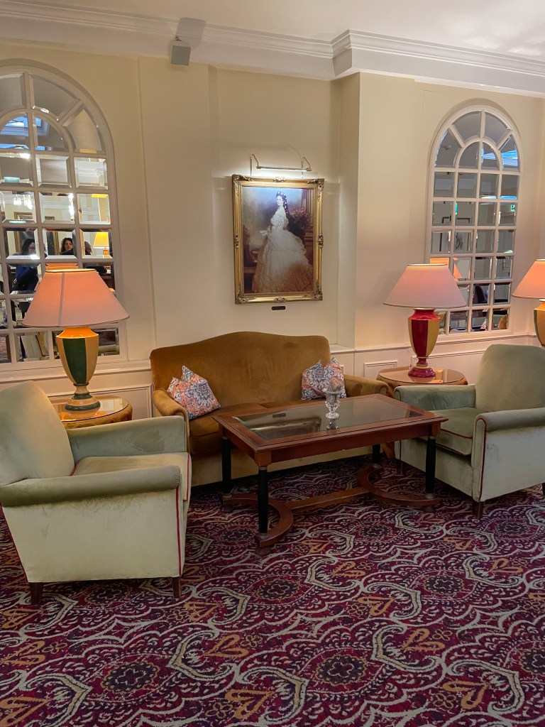 Una sala accogliente dell' Hotel Kaiserhof con divanetti verdi, tavolino in legno e lampade, decorata con un'opera d'arte appesa alla parete.