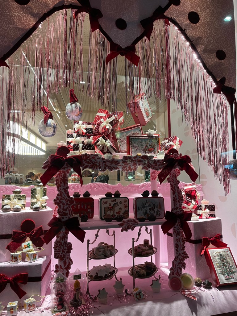 Vetrina natalizia decorata con dolci e regali, caratterizzata da un design festivo con nastri rossi e bianco, allestita per evocare l'atmosfera delle festività a Vienna.