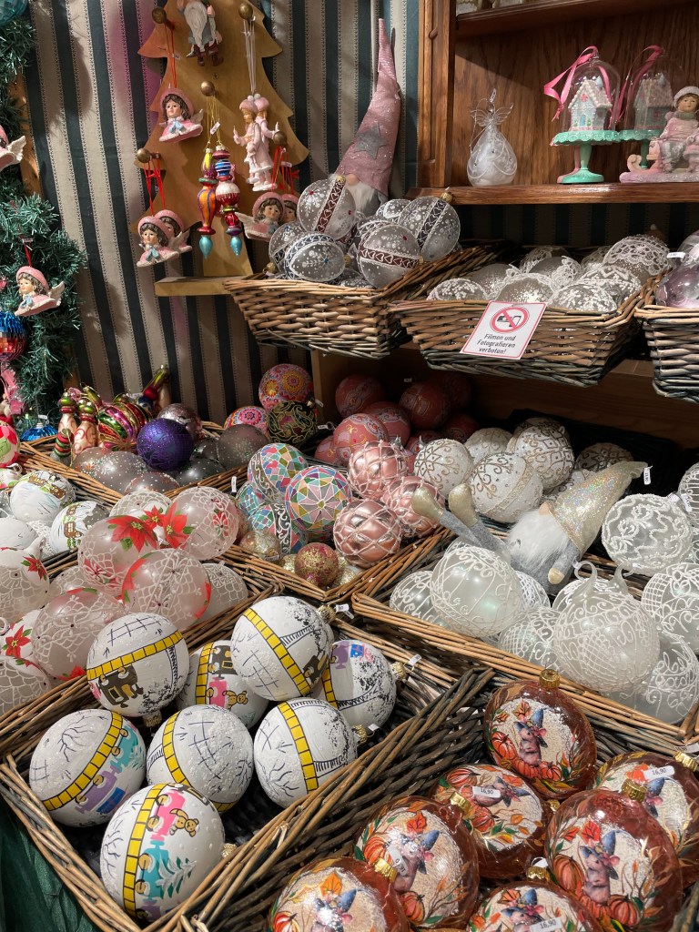 Un bancone di mercatino natalizio di Vienna con decorazioni natalizie come palline di vetro colorate e ornamenti artigianali, tra cui uova decorate e piccole figure natalizie.