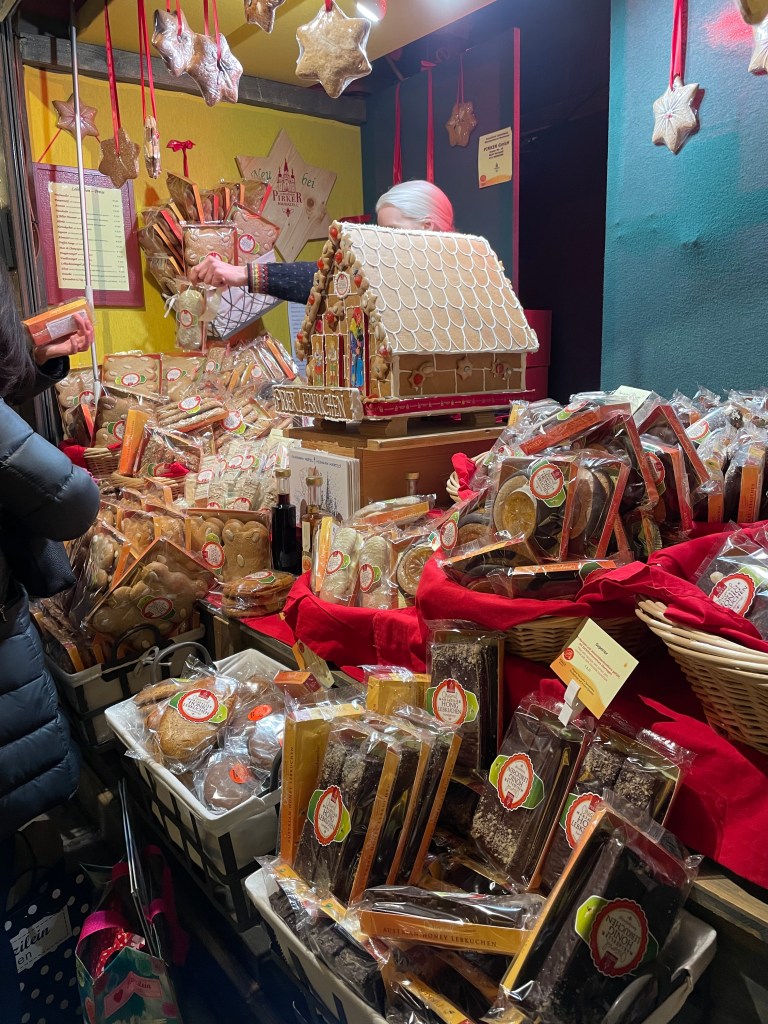 Ripiano di un mercatino natalizio a Vienna con una varietà di dolci tradizionali, come biscotti e pan di zenzero, esposti in cestini e su un bancone decorato.