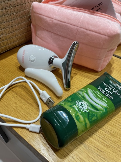 Un kit di bellezza che include un dispositivo per il viso, un tubo di gel all'aloe vera, un cavo USB e una borsa rosa.