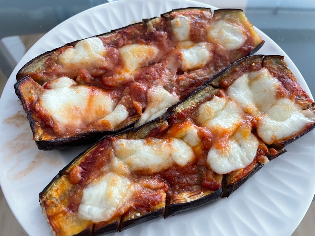 Melanzane alla parmigiana su un piatto bianco, con salsa di pomodoro e mozzarella fusa.