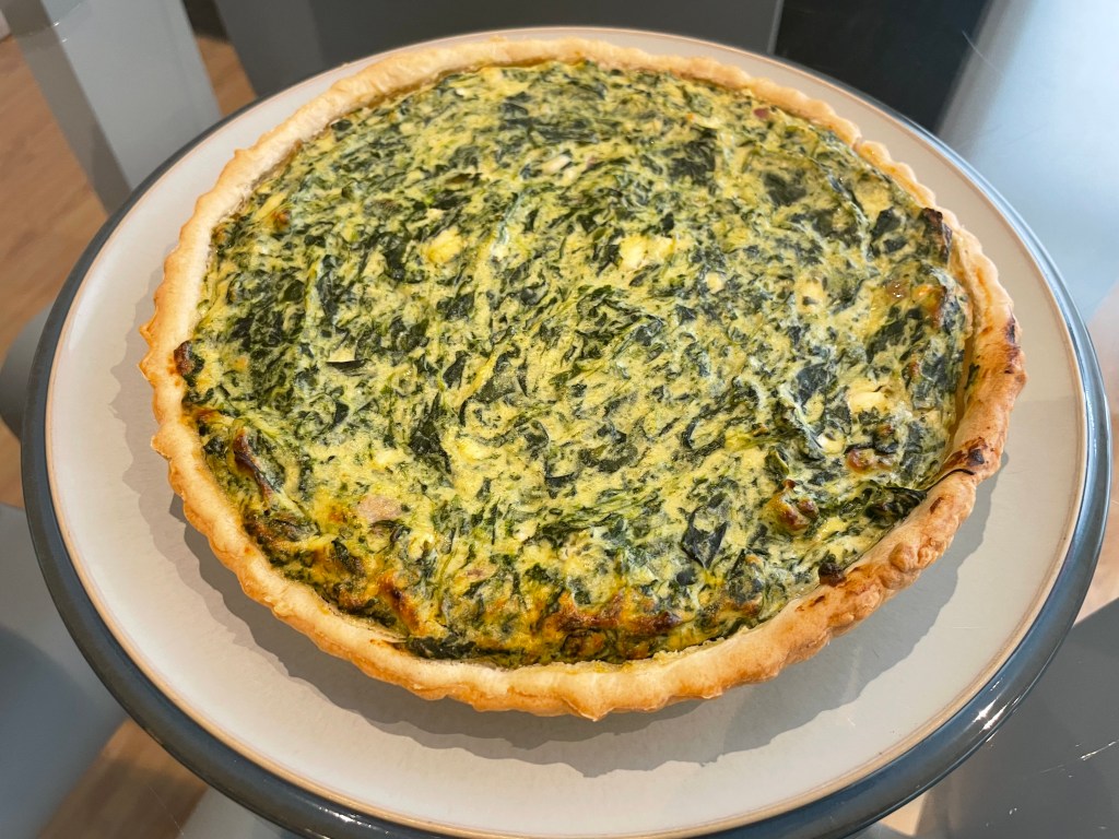 Una torta salata a base di spinaci e formaggio, servita su un piatto bianco.
